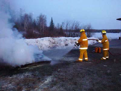 Two firefighters spraying water on an outdoor fire